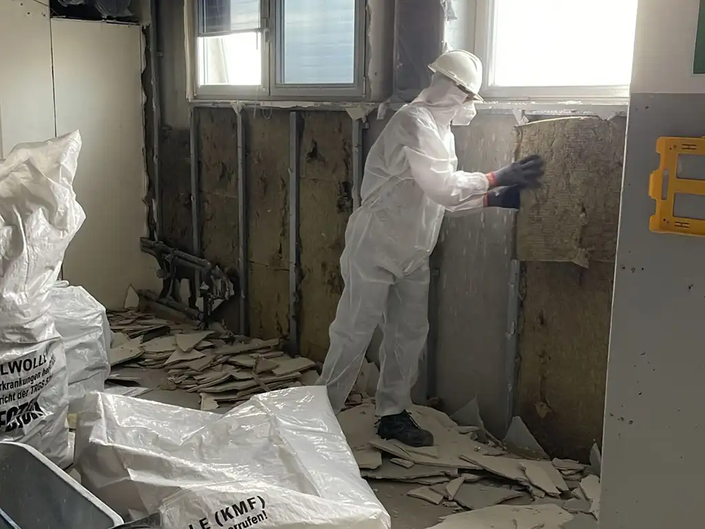 Arbeiter entfernt Mineralwolle bei Entkernungs- und Sanierungsarbeiten