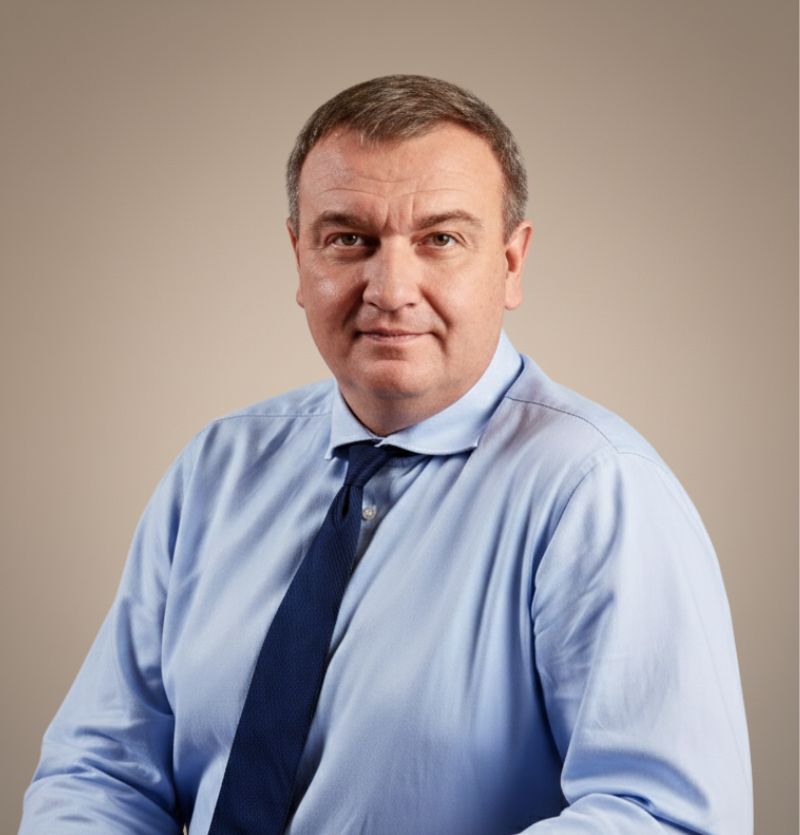 A confident person with short, styled hair and a leather jacket poses against a dark backdrop.