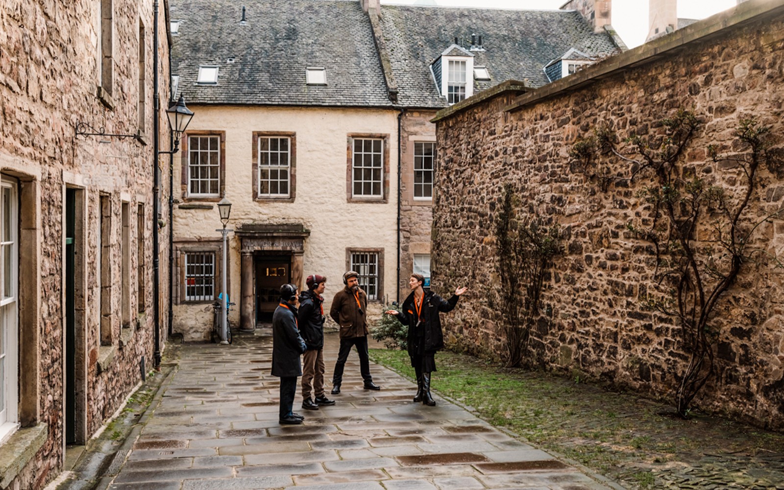 Tour group on Royal Mile, Edinburgh, listening to a guide near historic stone buildings.