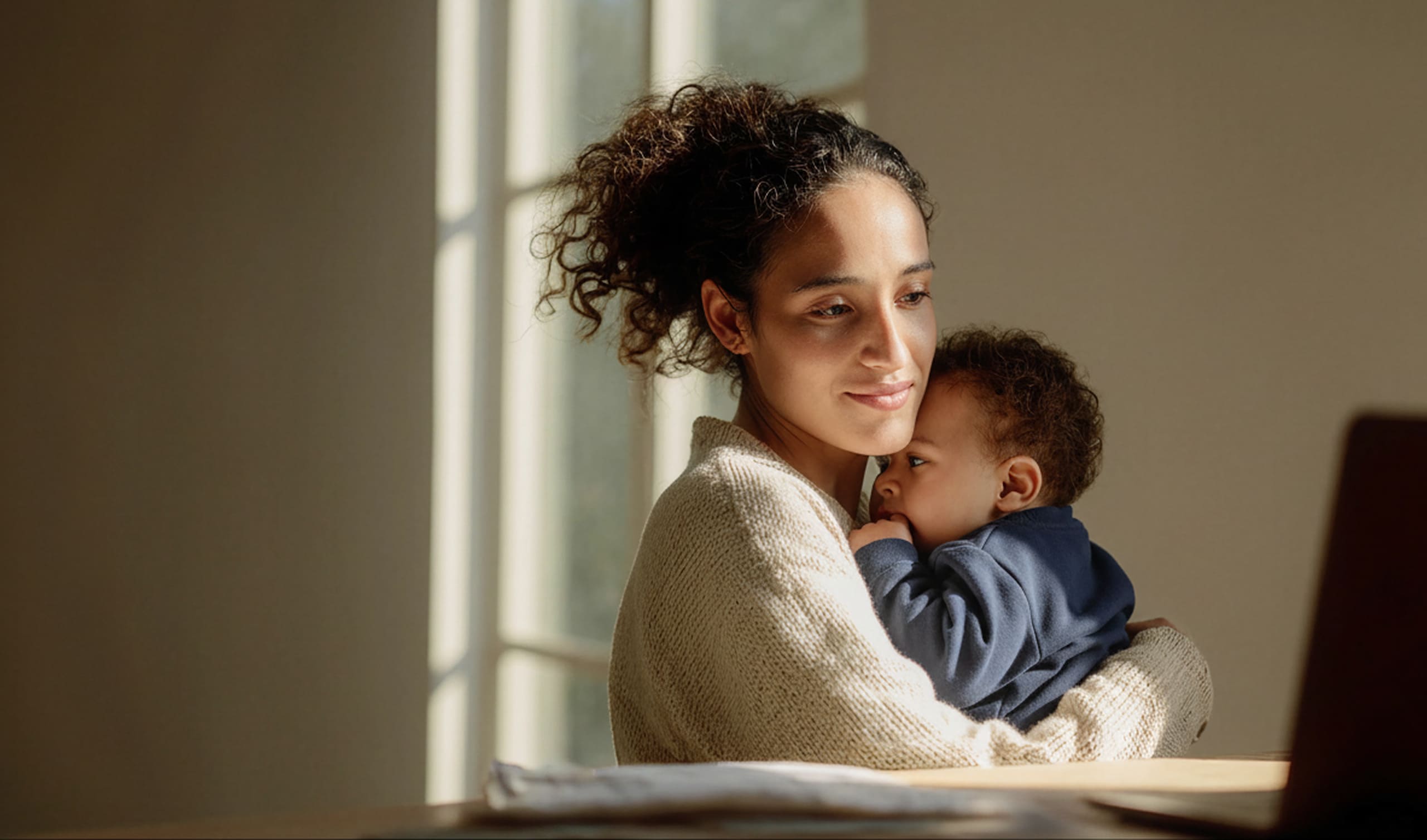 A young mother holding her toddler while having a telehealth call