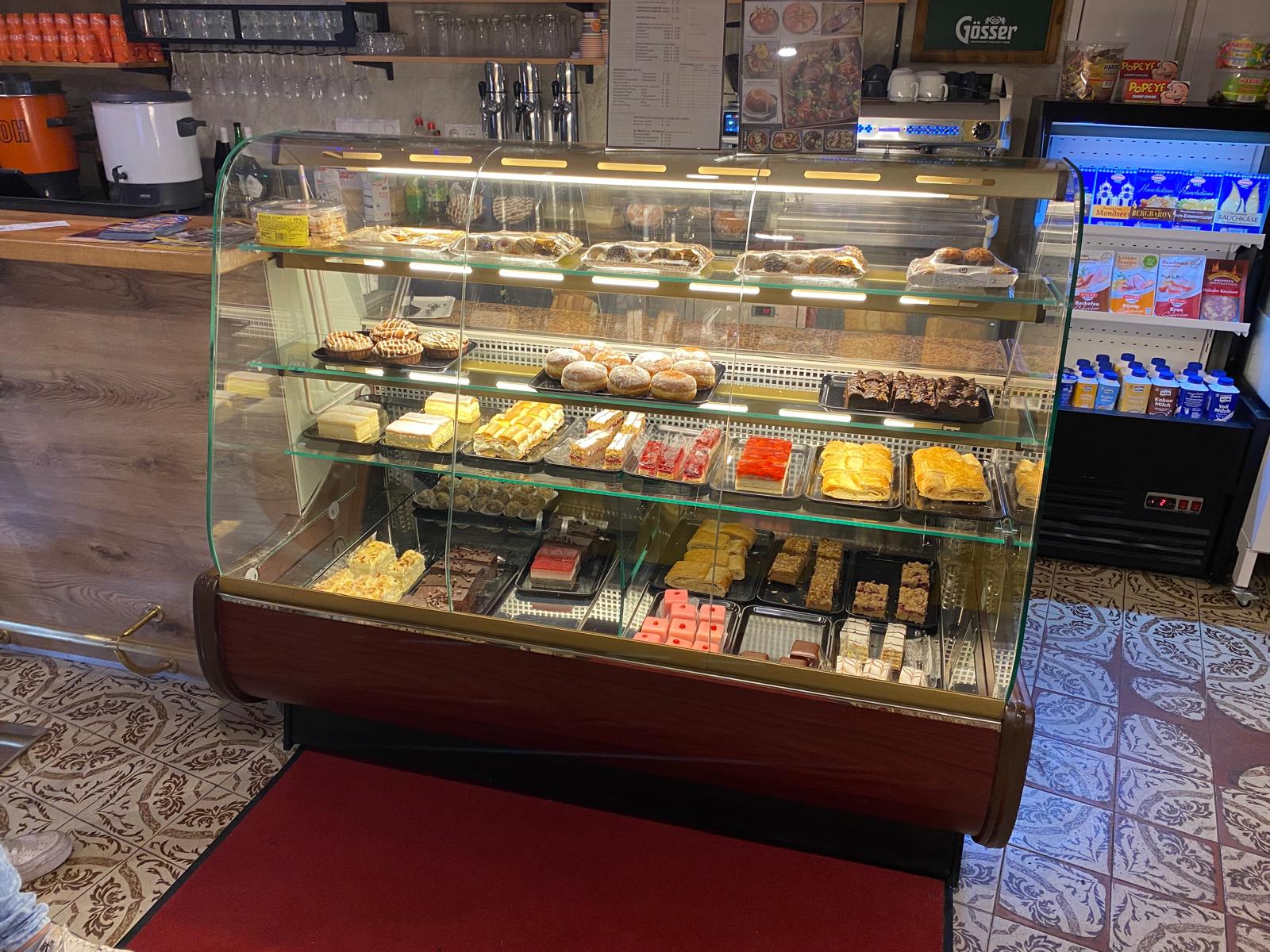 White plate with roasted carrots served on green sauce, topped with almonds and fresh herbs, held by a hand over a dark table.