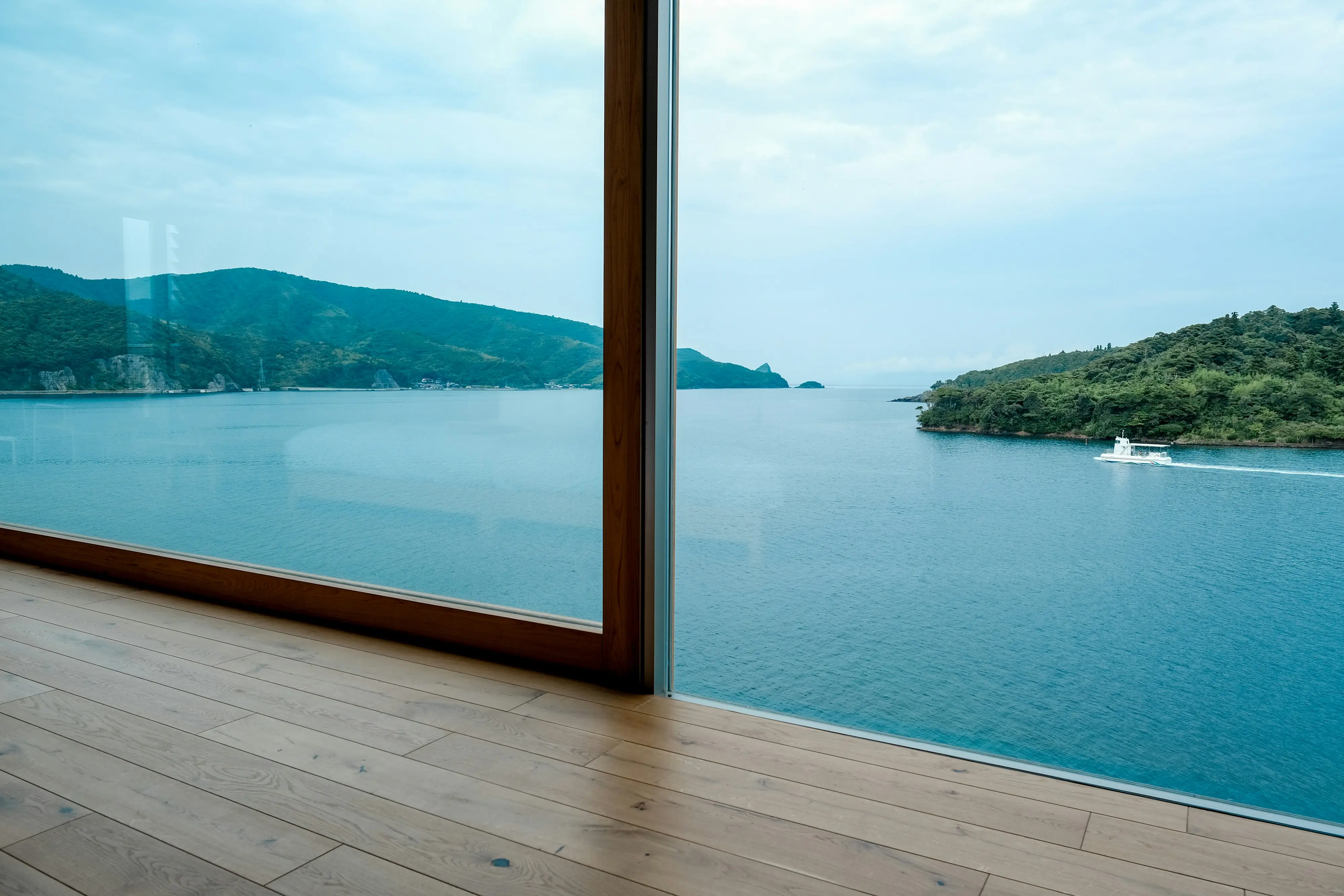 Inside a room, a large glass window frames an ocean view, showcasing the blue water and distant horizon.