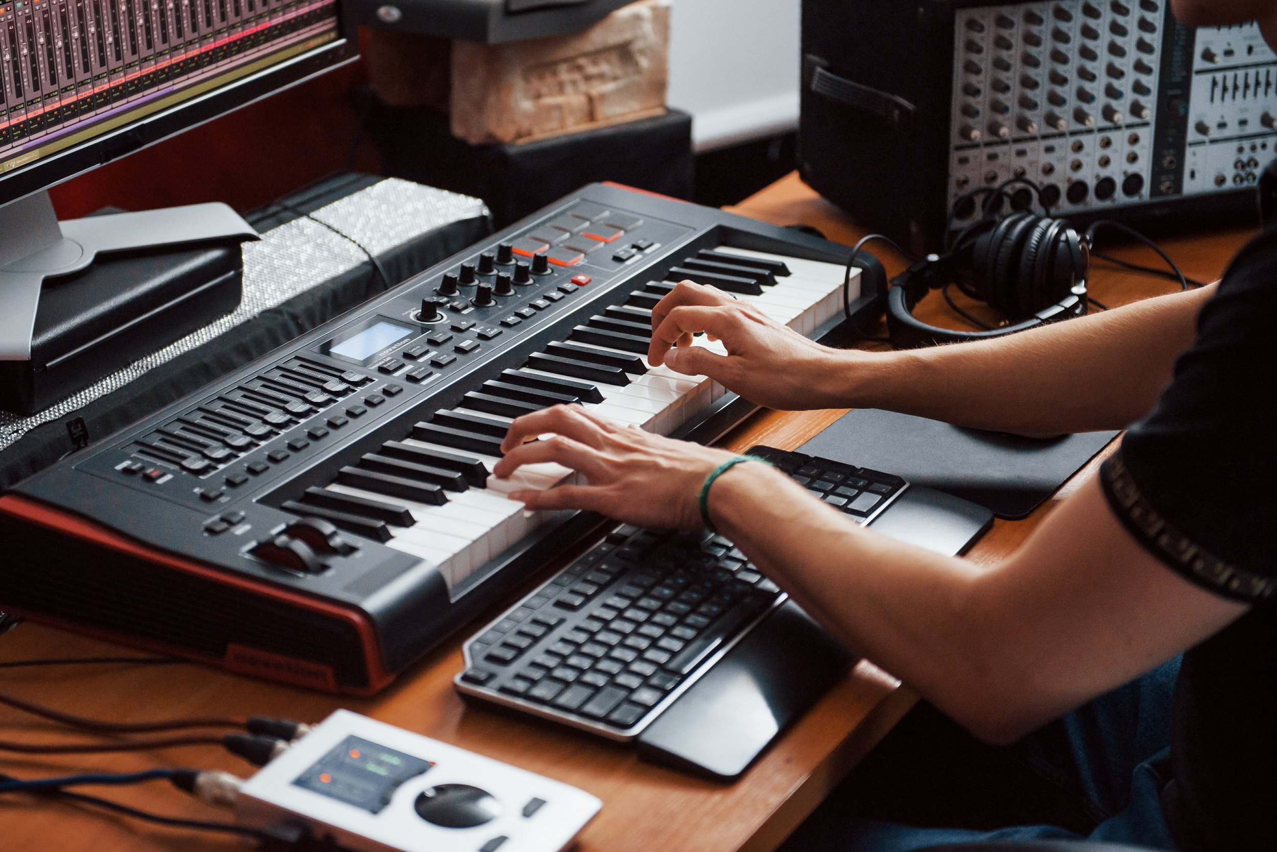 A person playing a keyboard at a workstation with screens, speakers and audio equipment.