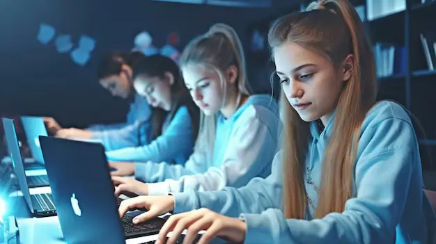 Teen girls focused on coding at laptops in a tech classroom, showcasing STEM education, programming skills, and hands-on computer science learning.