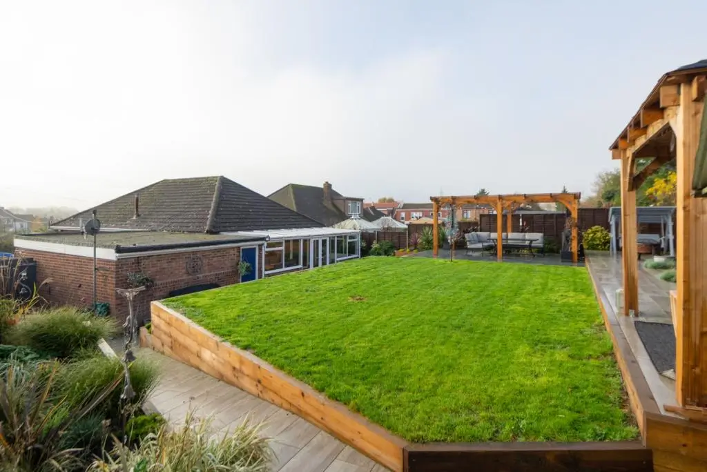 A spacious garden with green grass, surrounded by hills and a wooden structure in the foreground.