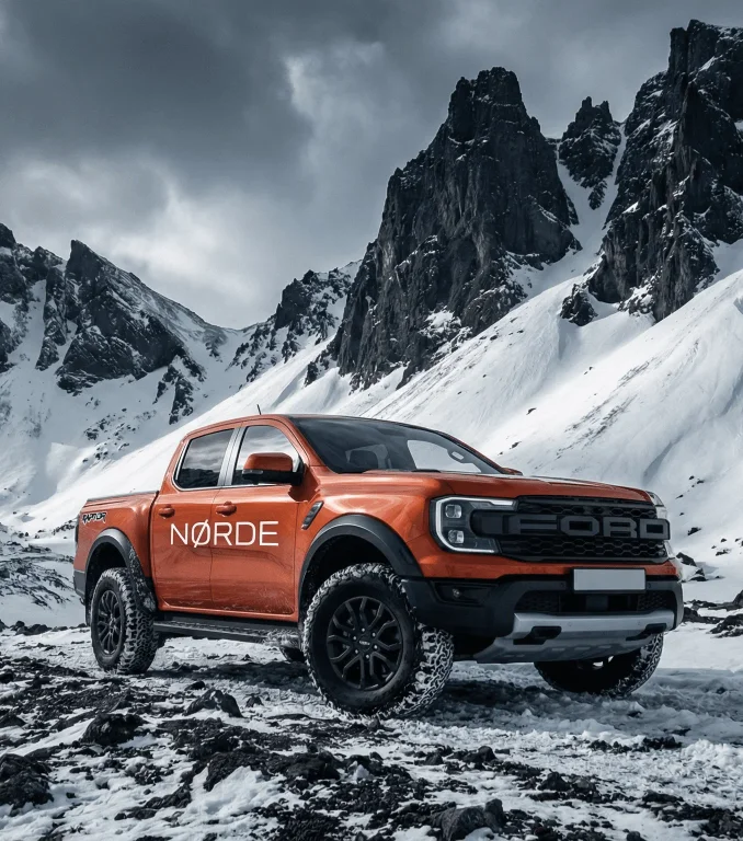 A rugged orange SUV parked in a snowy landscape with dramatic mountain peaks in the background.