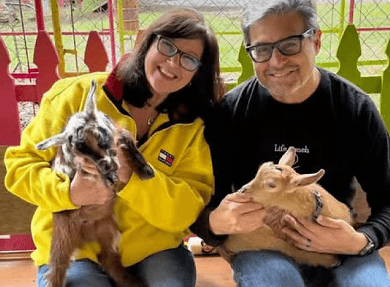 a man and women looking to camera and in hand have a 2 goat baby.
