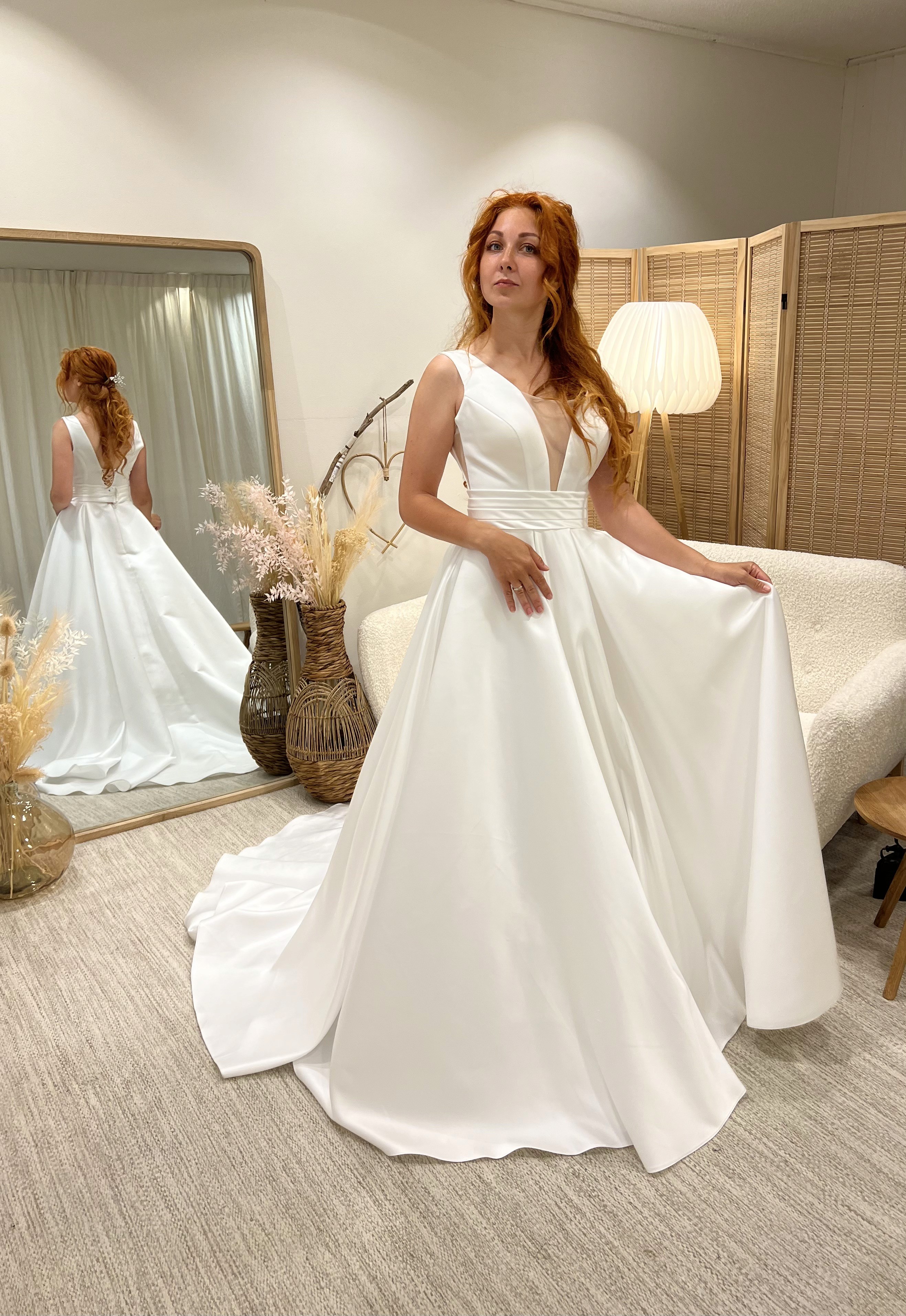 Minimalistische trouwjurk van satijn met diepe V-hals en wijde rok, gepresenteerd in Magnolia Bruidsatelier in Deventer – verkrijgbaar voor verhuur of op maat gemaakt.