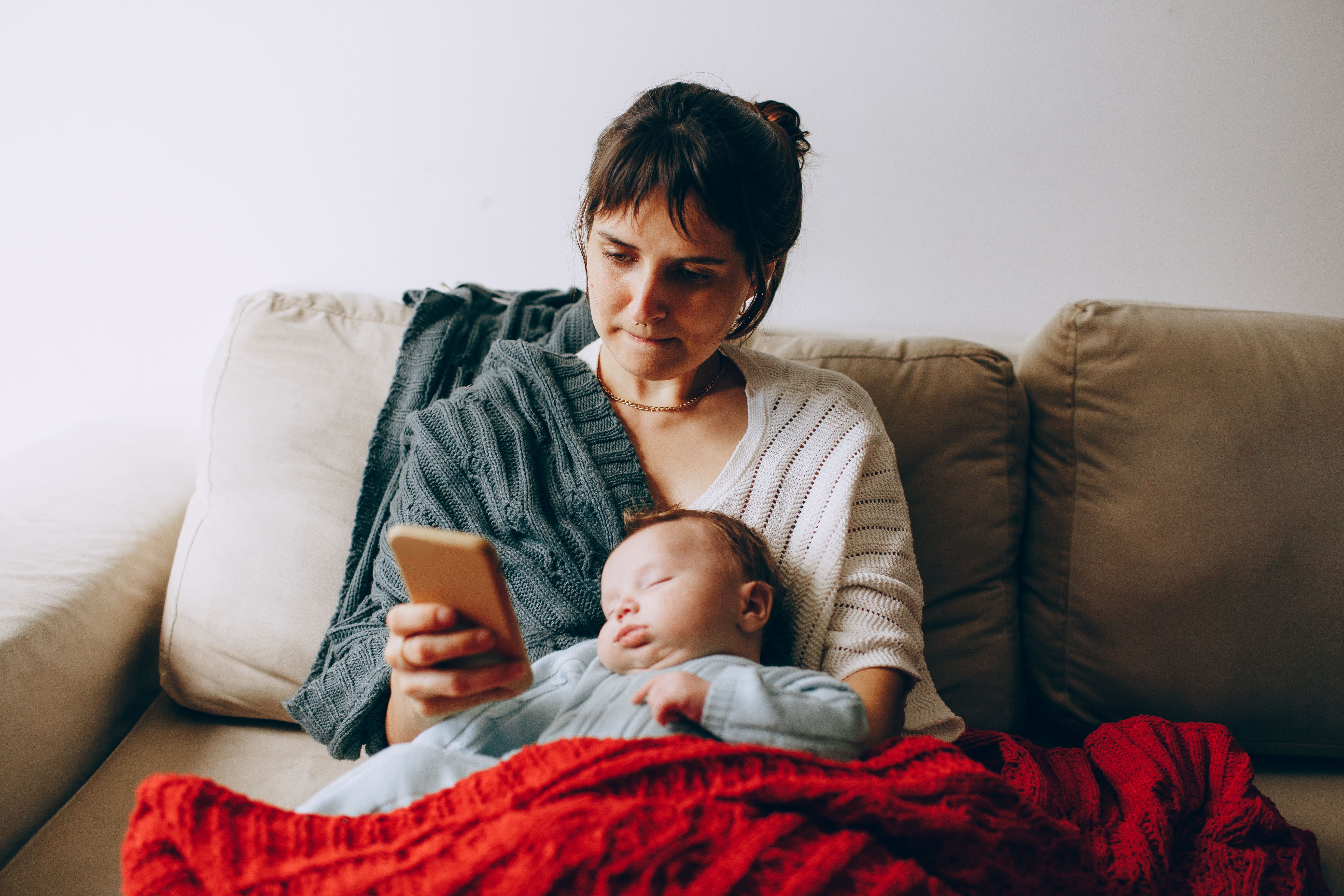 a-serene-moment-with-a-mother-browsing-her-phone-as-her-baby-sleeps-on-the-couch - helena-lopes (pexels)