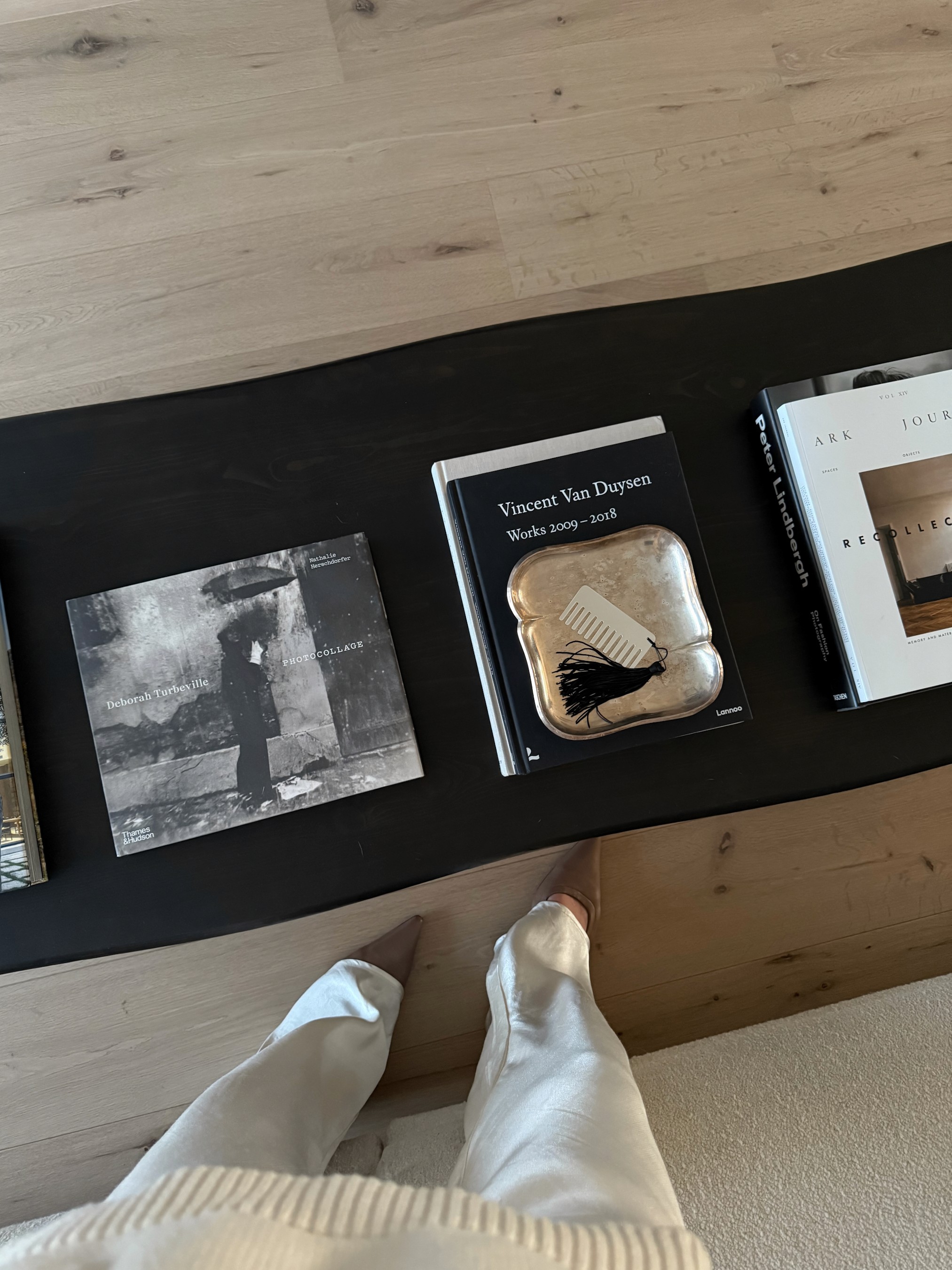 Black coffee table styled with architecture and design books including Vincent Van Duysen monograph, bronze tray, and bone comb