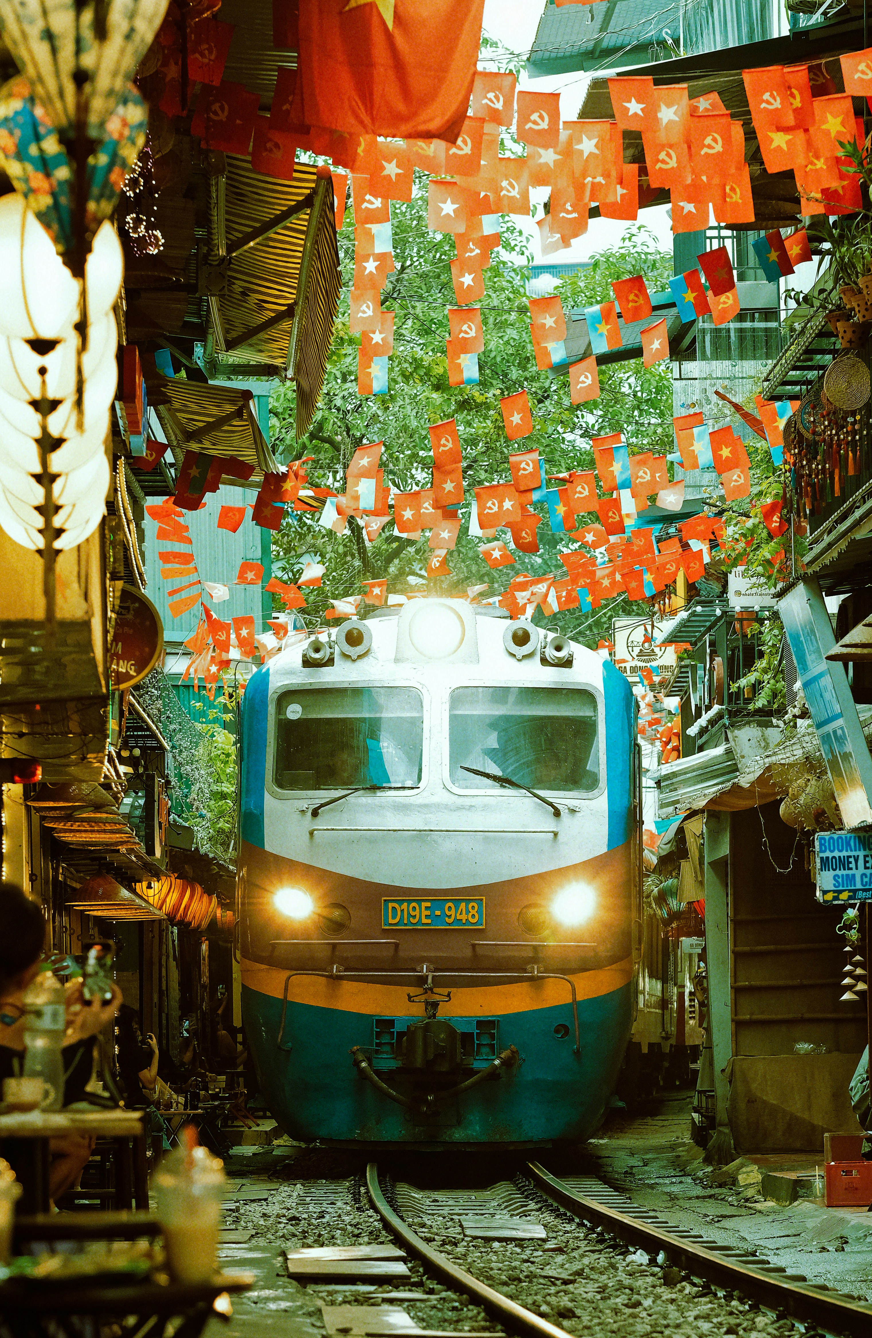 Train passes through a narrow street decorated with flags.