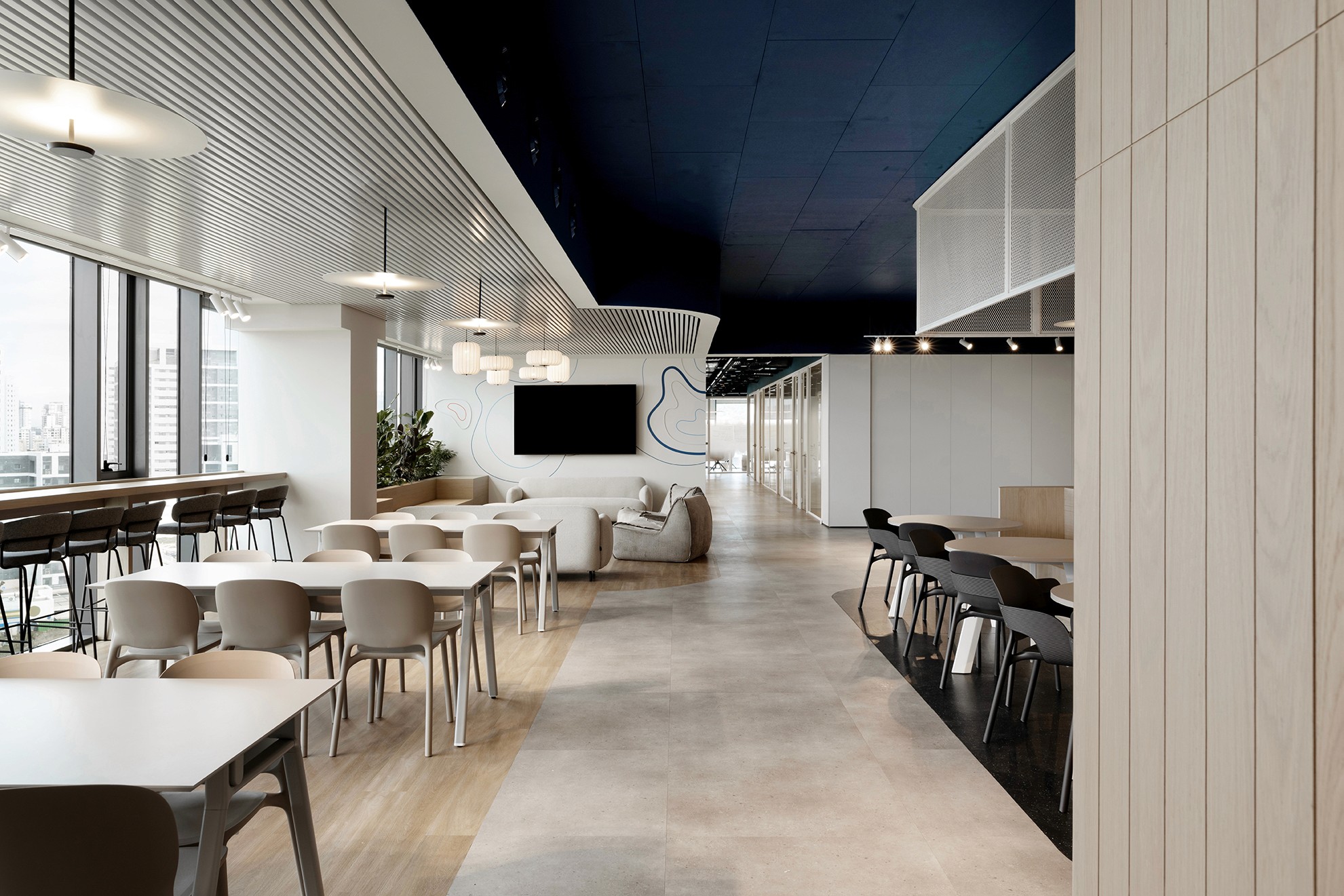 אזור אכילה בקו ראשון לים – שילוב תקרה אקוסטית לינארית (Linear Baffles) בלבן עם מערכות חשופות בכחול תעשייתי