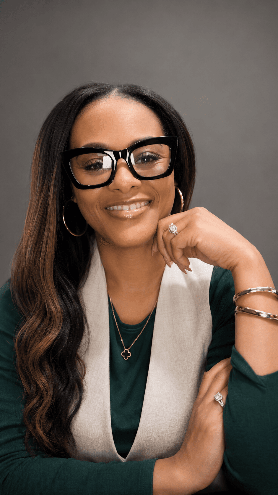 Portrait of PlateWise Health founder Shemira Shaw smiling, wearing black glasses and jewelry against a neutral background.