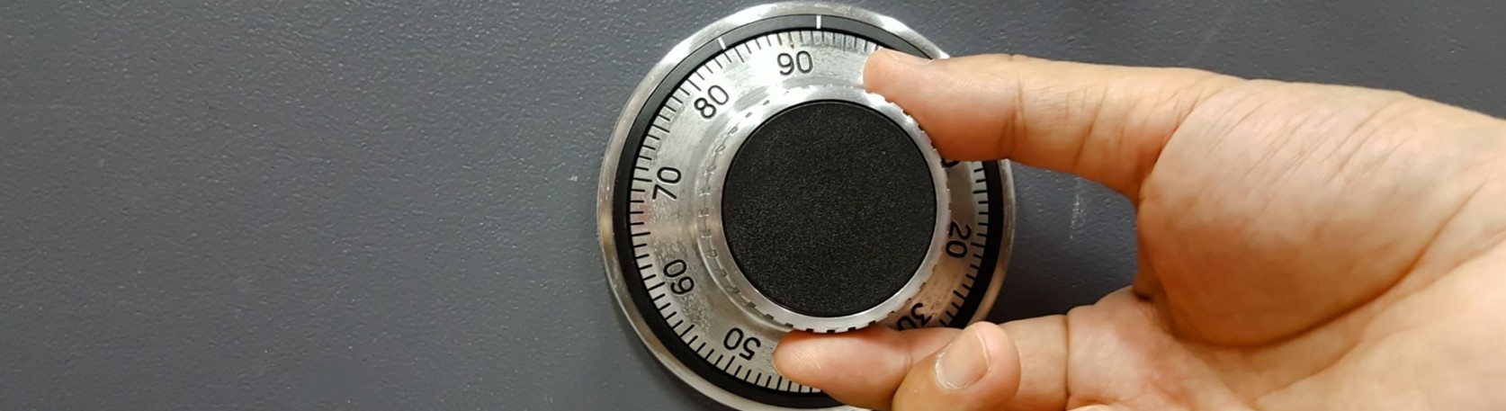 Close-up of a man's hand dialing a mechanical combination lock on a safe, focusing on the dial.