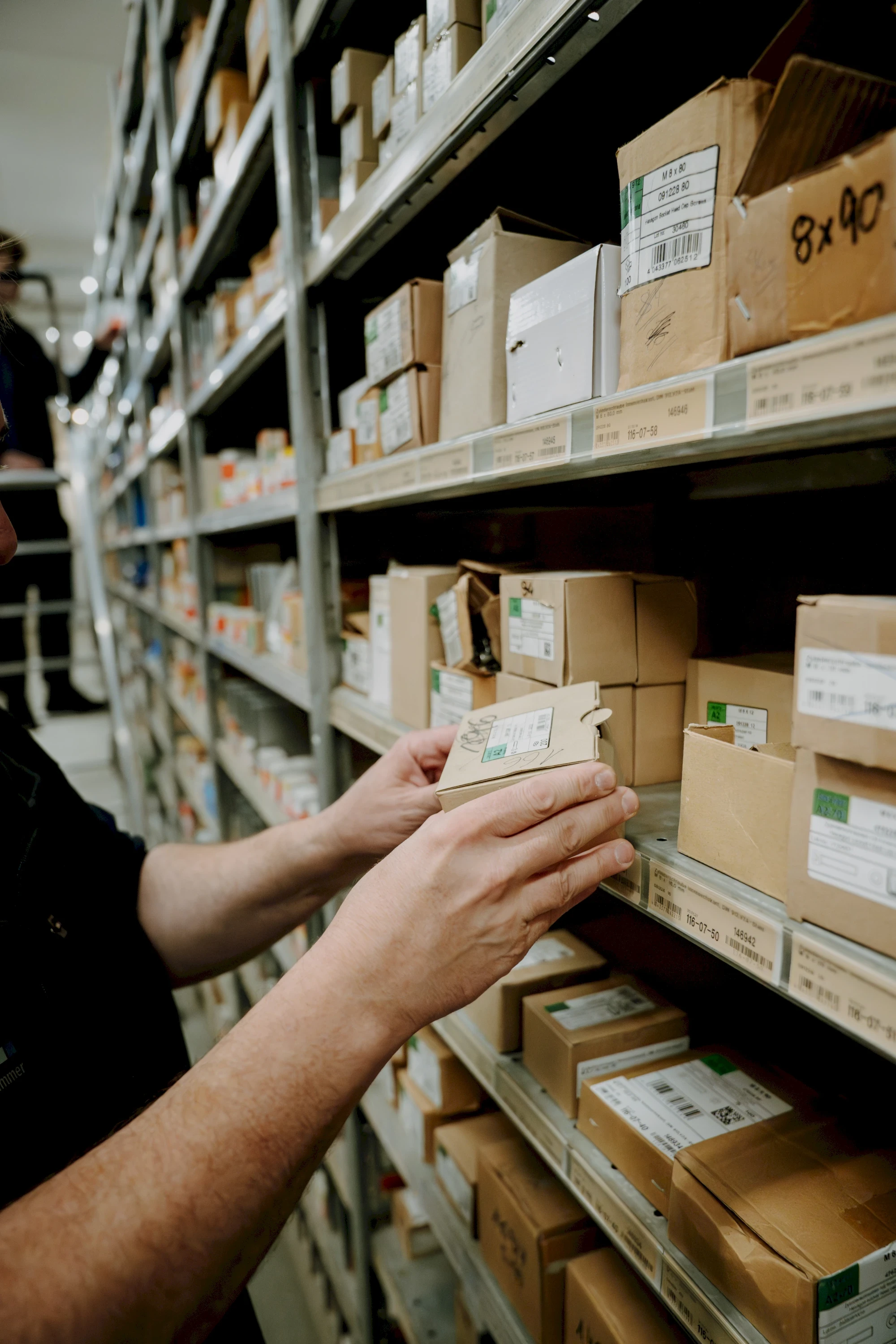 Person betrachtet Schachtel in Regal. Geordnetes Lager mit vielen Kisten und Boxen für Waren. Industrie und Logistik.