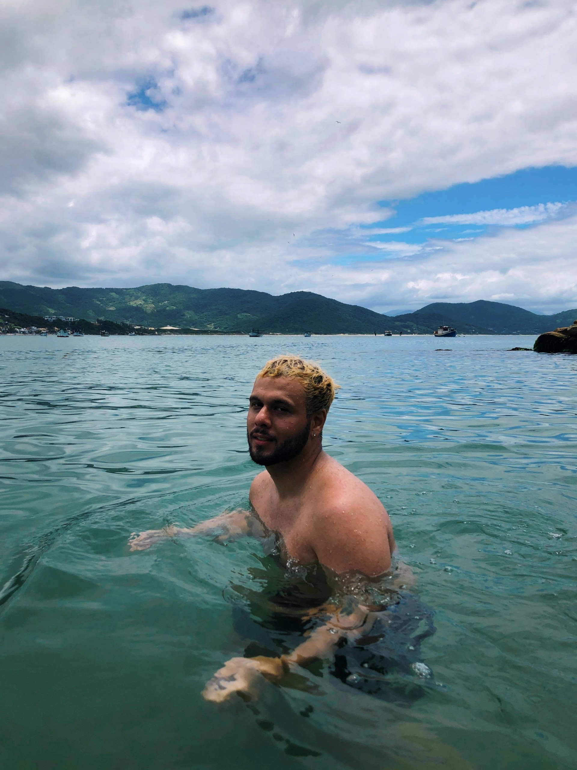 A view from an airplane window shows the aircraft's wing with a golden hue reflecting the setting sun, against a serene backdrop of fluffy clouds and a clear sky.