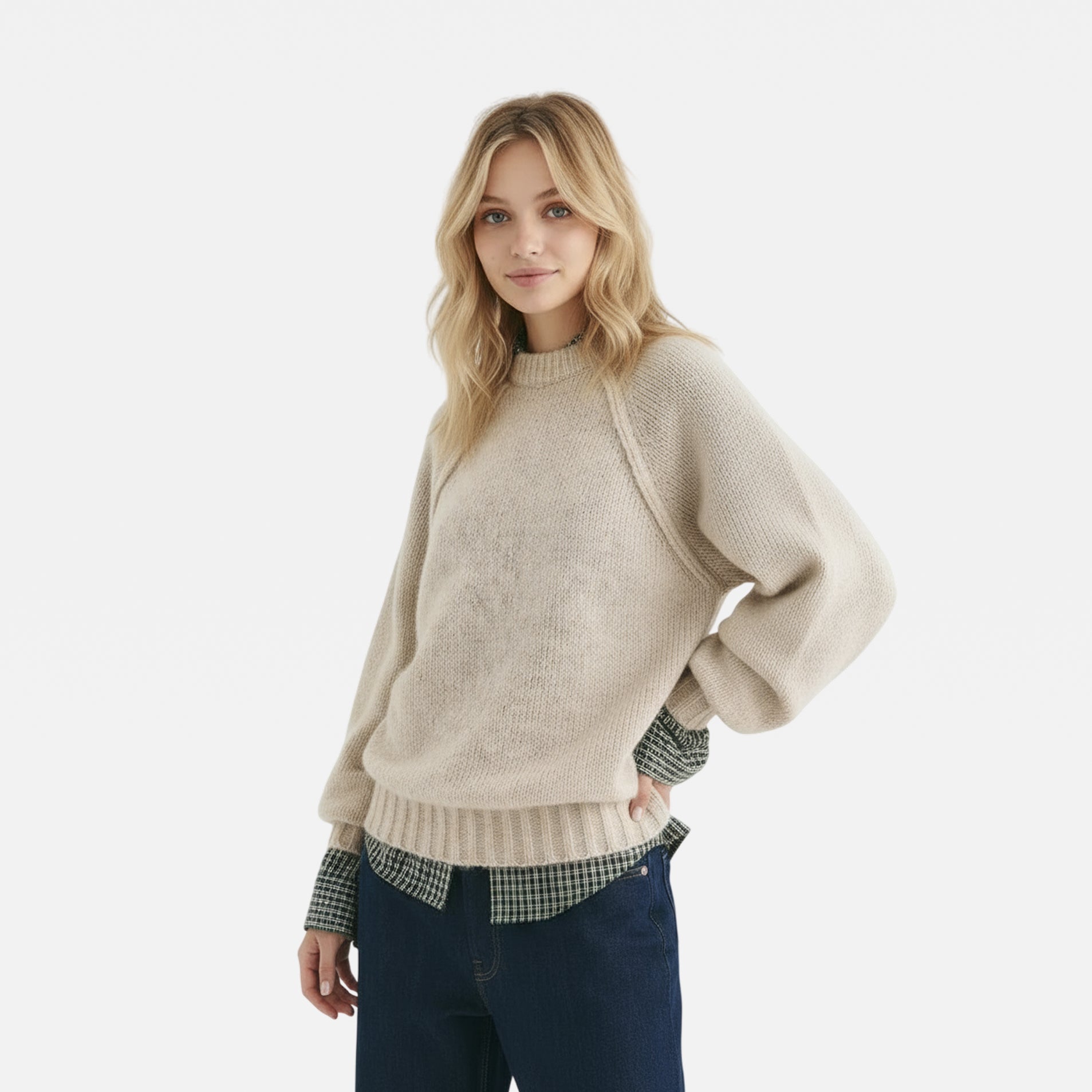 Woman wearing a beige sweater with a plaid shirt underneath on a white background