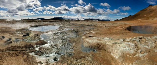 Steaming geothermal landscape at the Hverir geothermal area near Krafla in North Iceland, featuring bubbling mud pools, fumaroles, mineral-stained earth, and volcanic mountains under a dramatic cloudy sky.