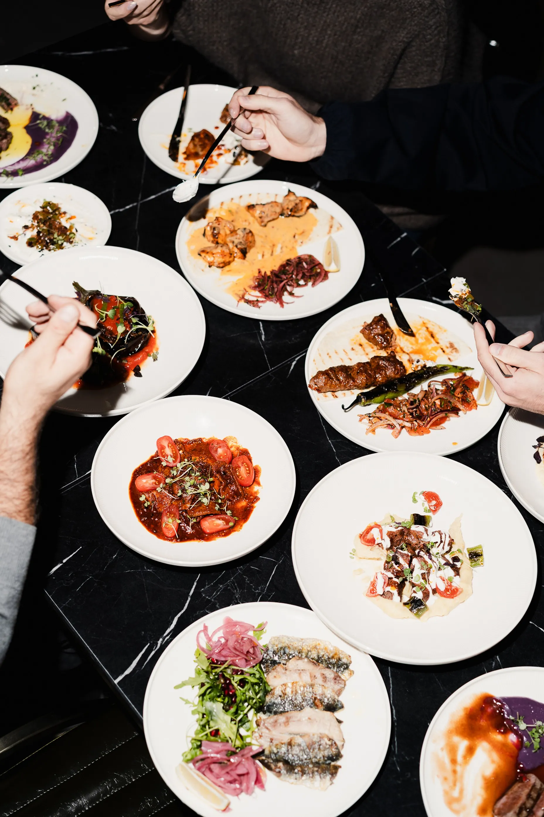 Das Mangal-Sharing-Dinner-Konzept, wie es leibt und lebt. Viele Teller am Tisch, Händ die reichen und teilen. Menschen die genießen.