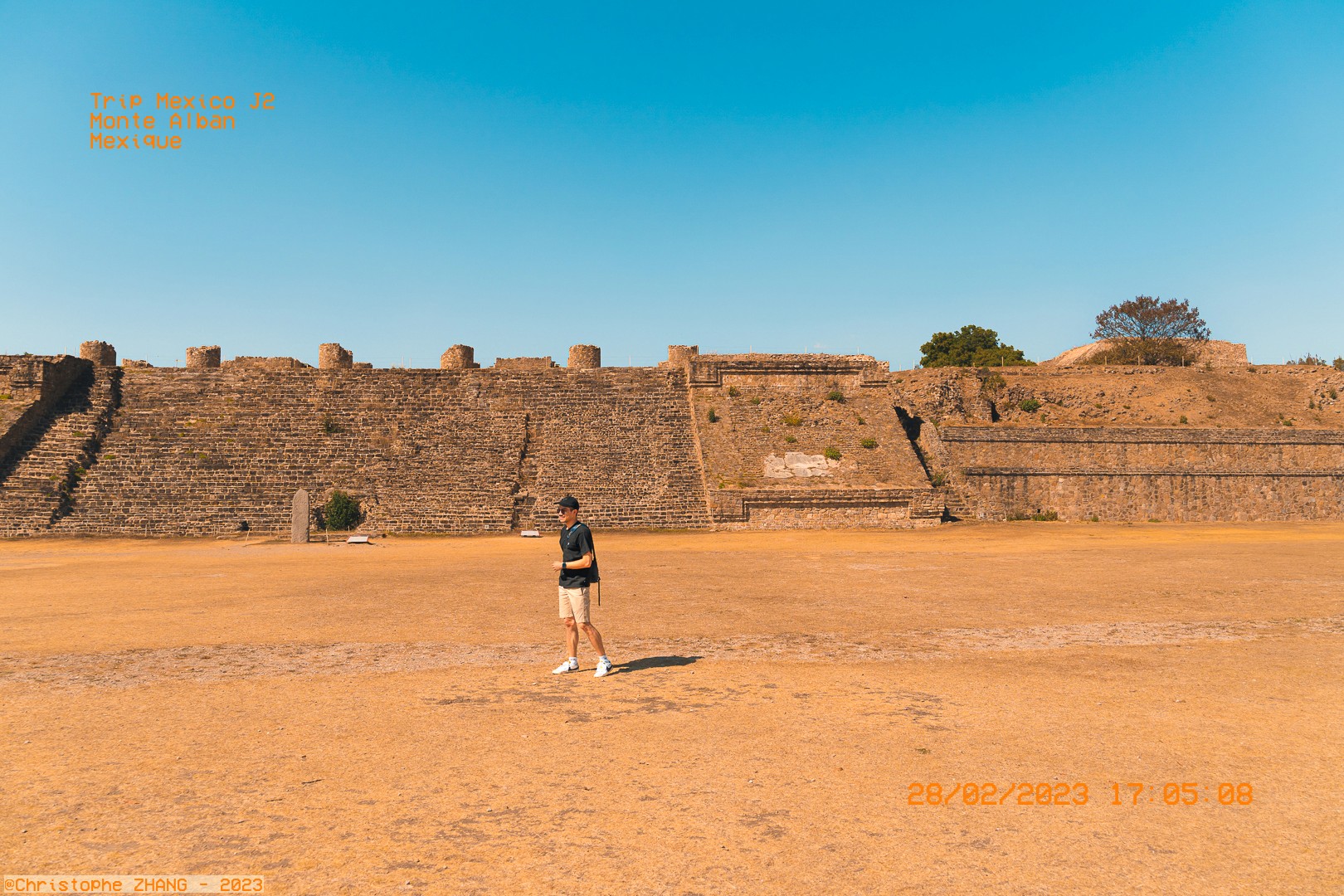 Visiteur explorant le site archéologique de Monte Albán sous un ciel bleu clair.