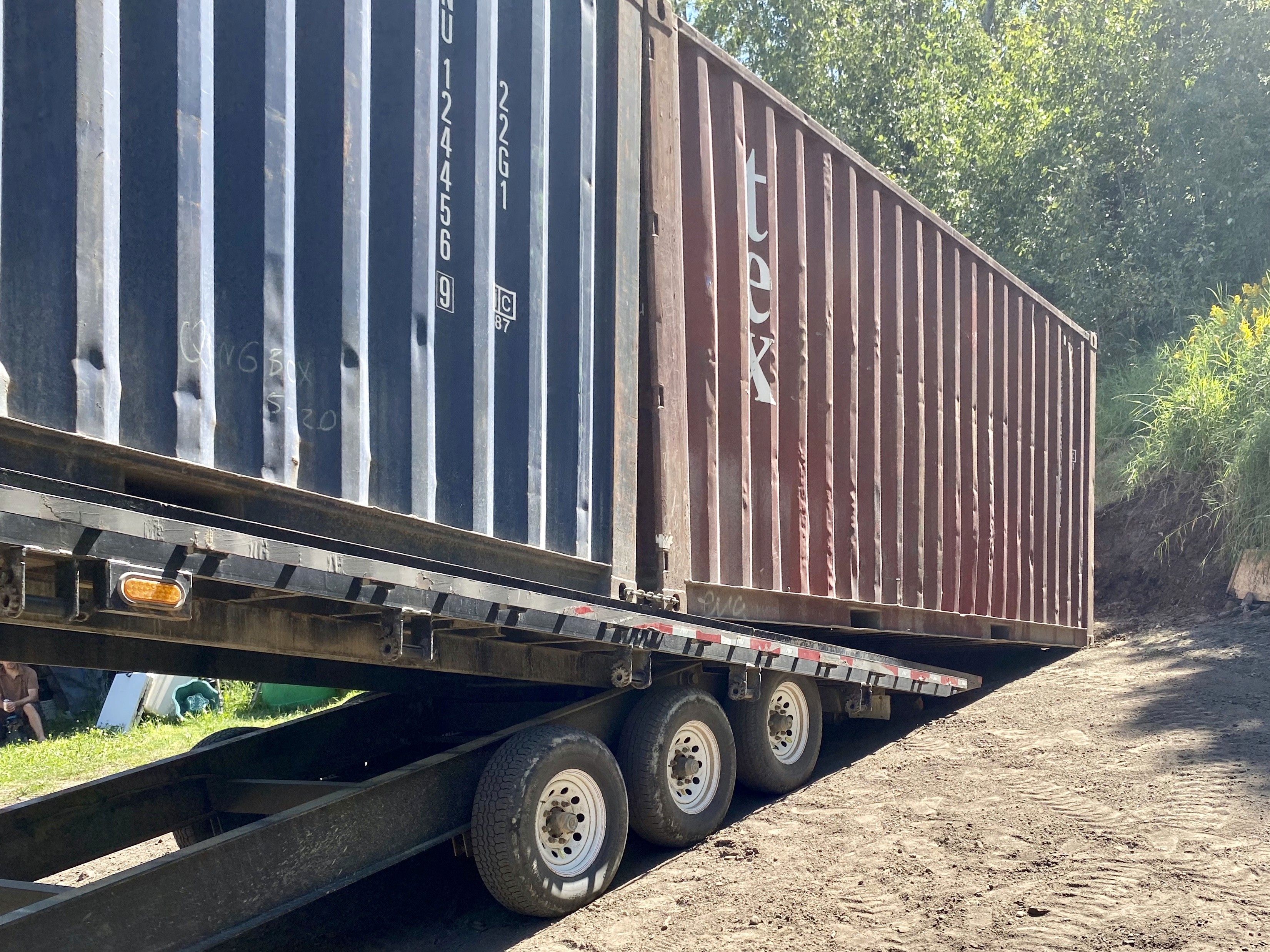 Two 20-foot used shipping containers being unloaded with a 40' tilt deck trailer