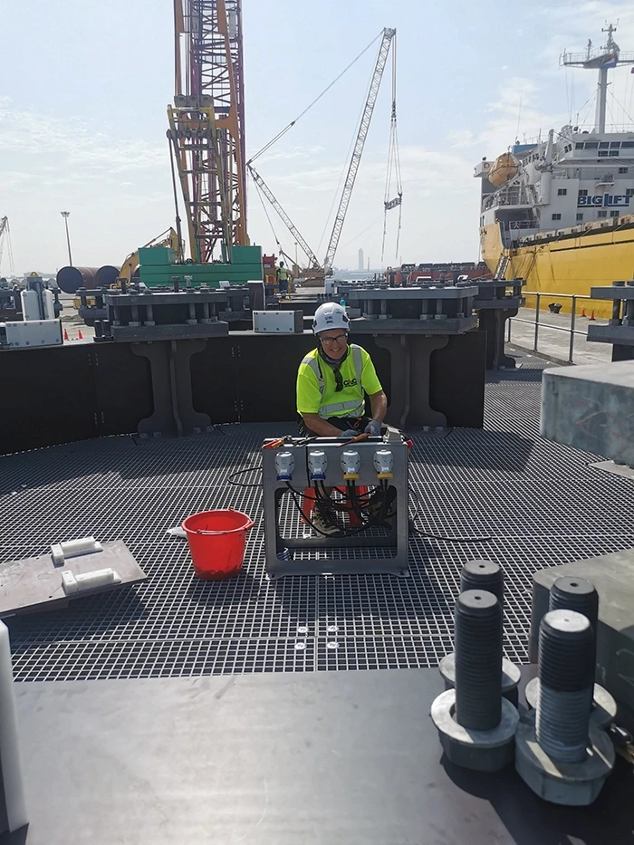 Engineer working on an offshore port deck surrounded by cranes and equipment.