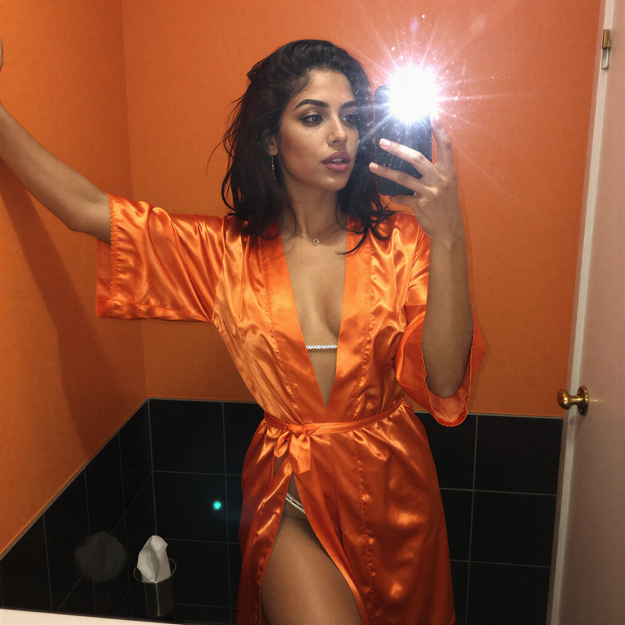 Woman in orange satin robe taking a mirror selfie with flash.