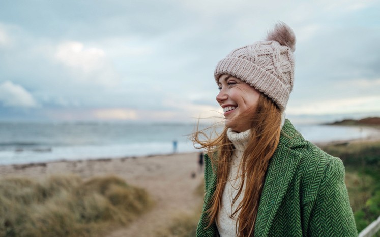 Smiling woman in warm clothing walking on beach