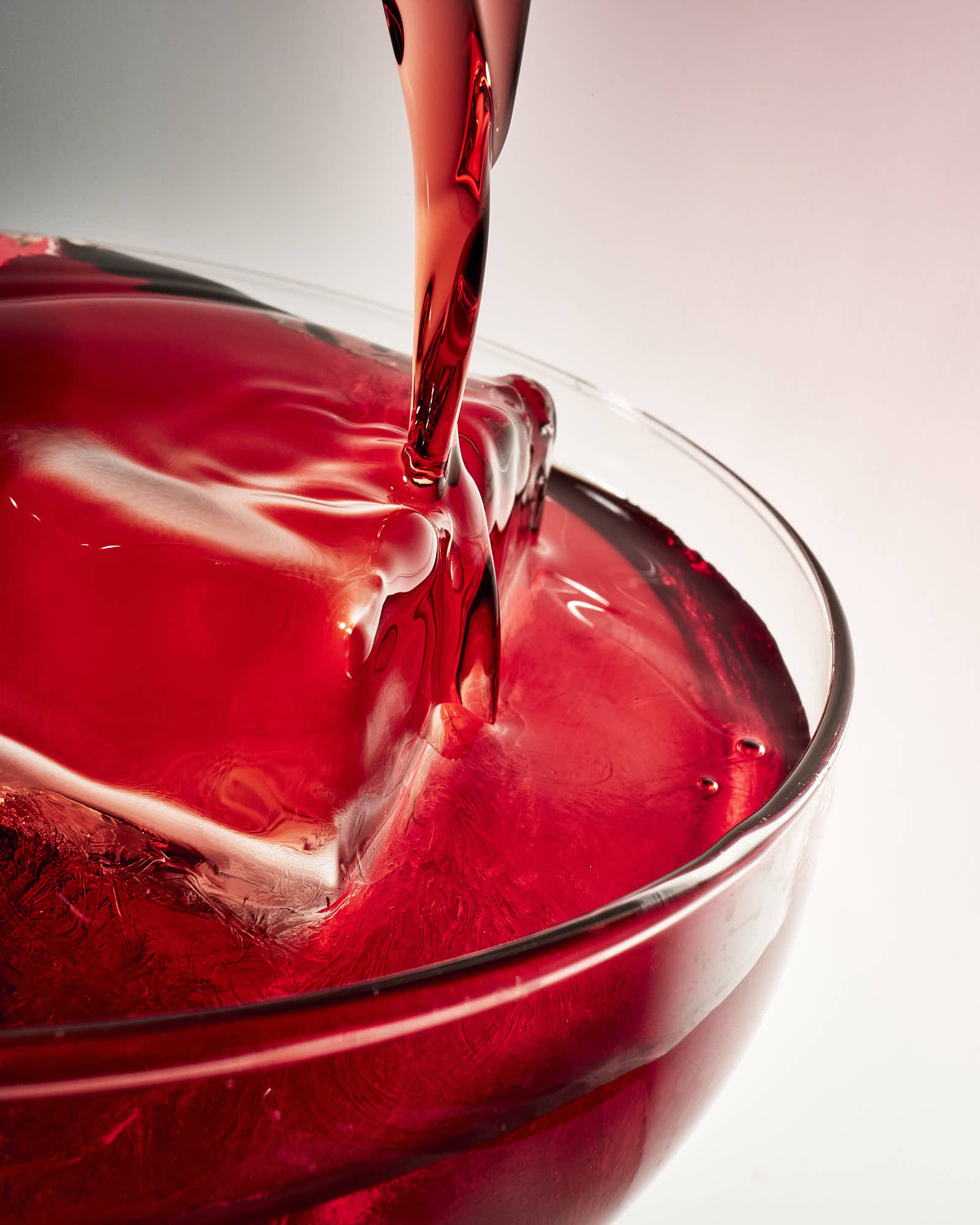 A close-up of a vibrant red liquid being poured into a glass, creating ripples and reflections.