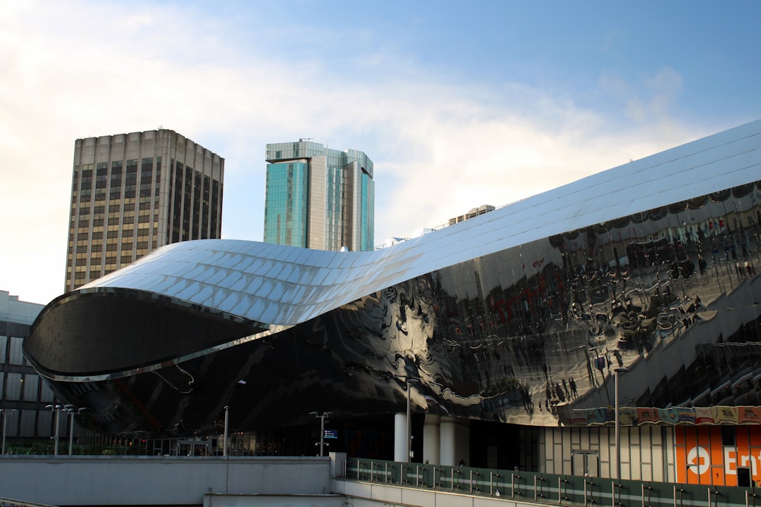 Modern curved mirrored building facade beside office towers under a partly cloudy sky.
