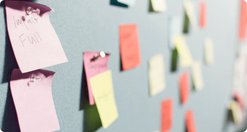 A wall or board covered in various colorful sticky notes or paper scraps, with handwritten text, creating a cluttered and disorganized composition that suggests a busy work environment.