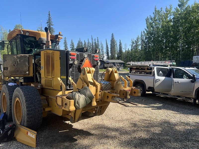 Rear view of a road grader being serviced for HVAC maintenance with a work truck in the background