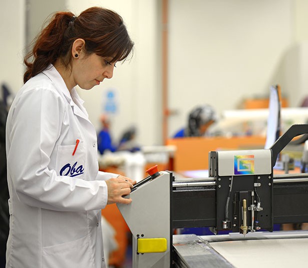 A man and woman sit on beige chairs in a modern room with a red paneled wall. A red pendant light hangs above a wooden coffee table between them.