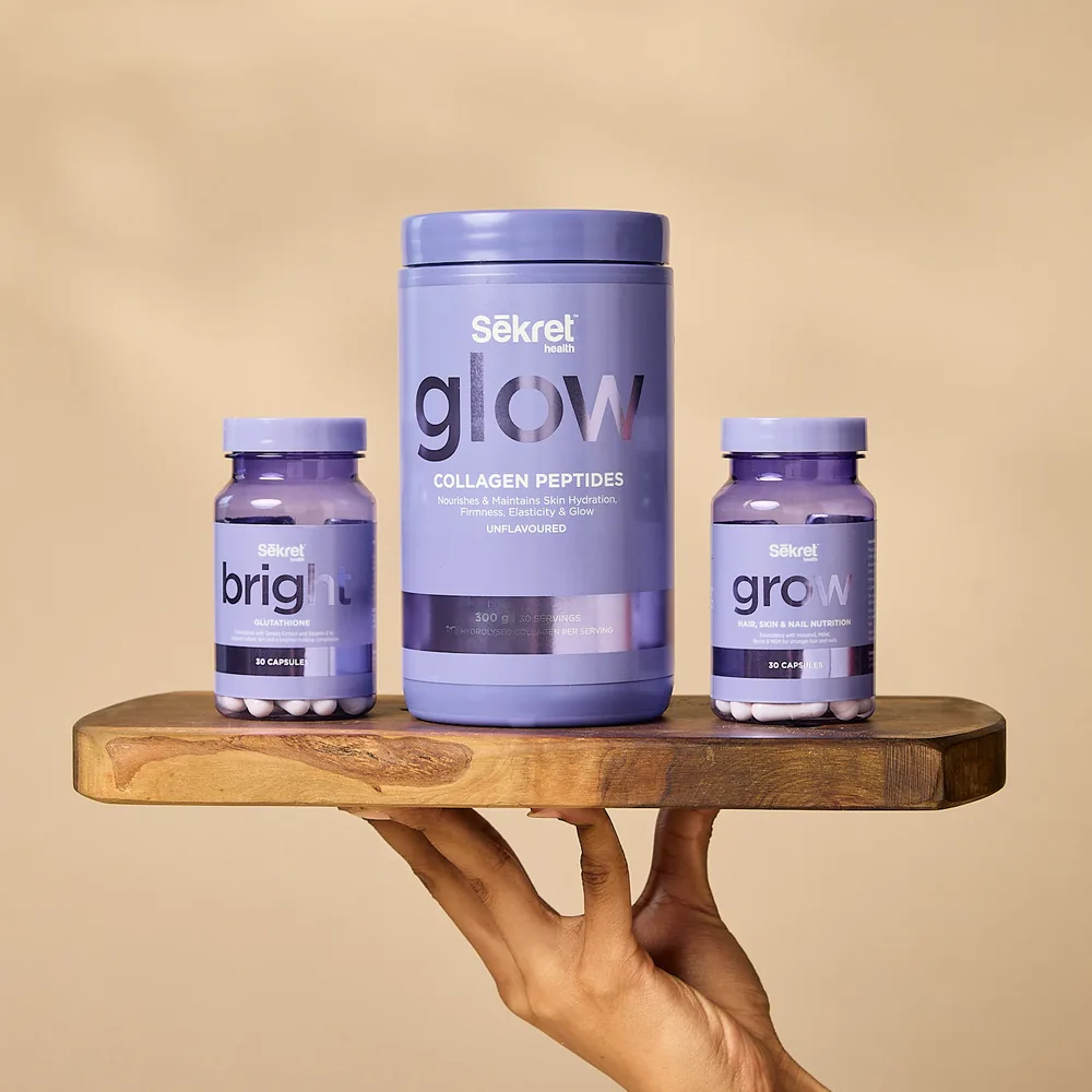 The Sēkret Glow collagen tub, Bright and Grow capsules on a wooden board held up by hand