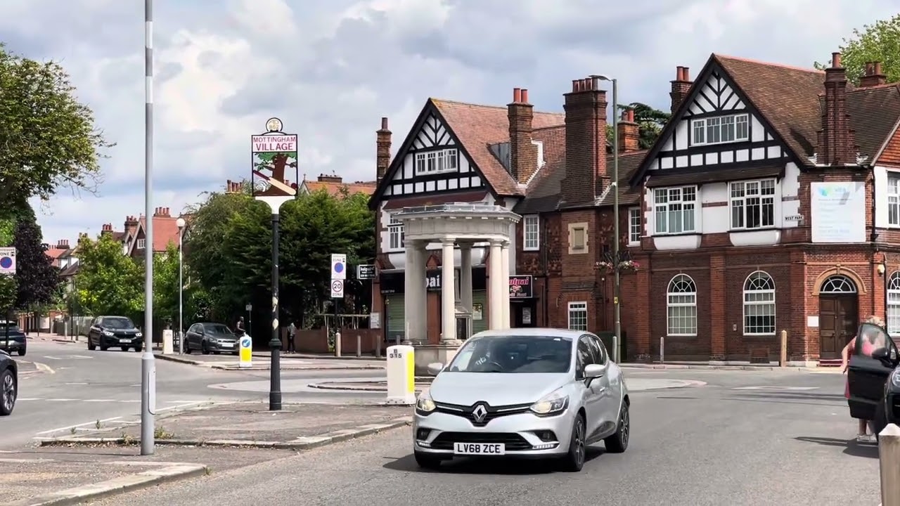 A smiling man with curly hair is sitting at a desk, looking at the camera, with a laptop and a lamp in the background.