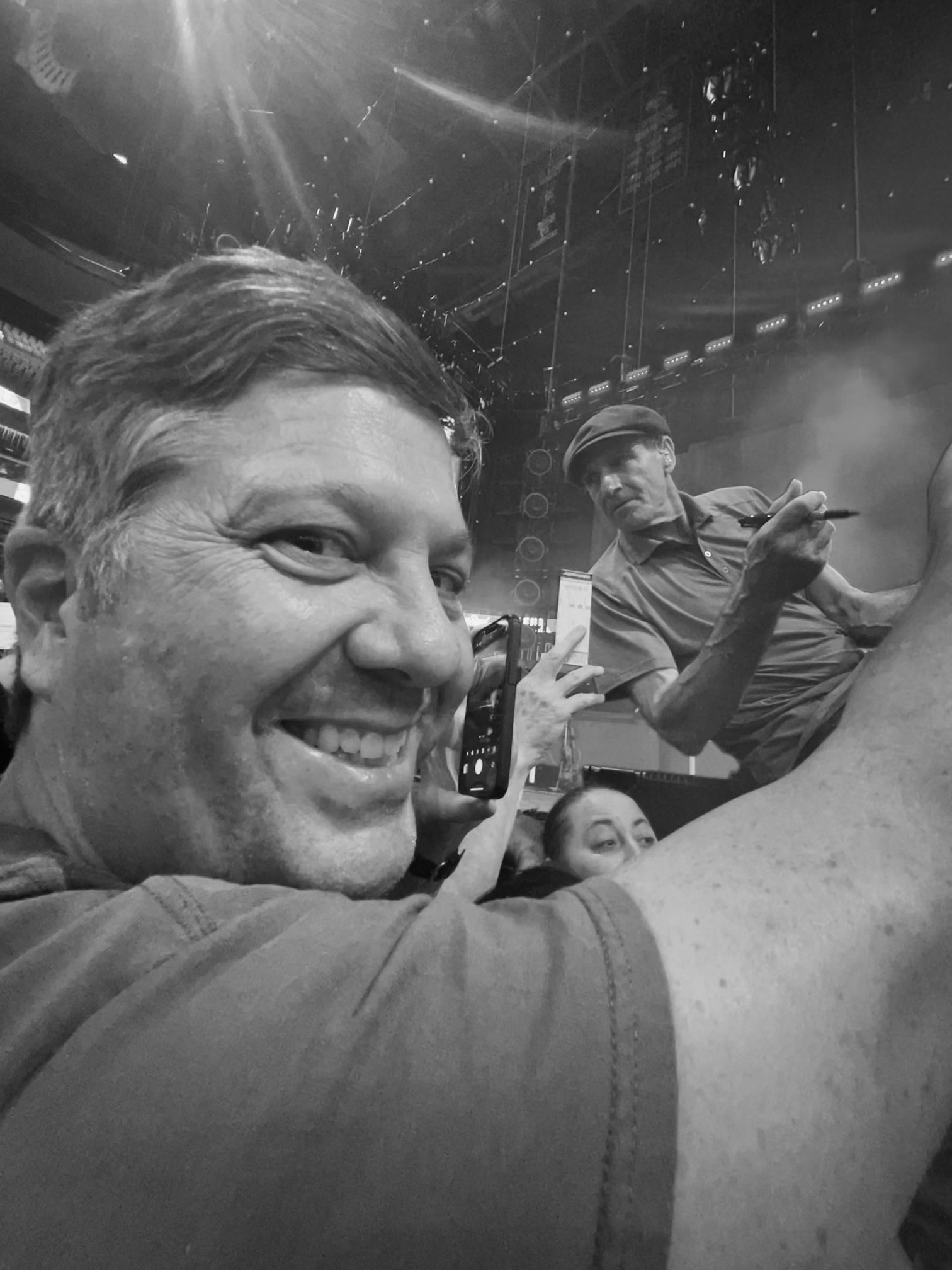 Man smiling in the foreground with James Taylor signing autographs in the background