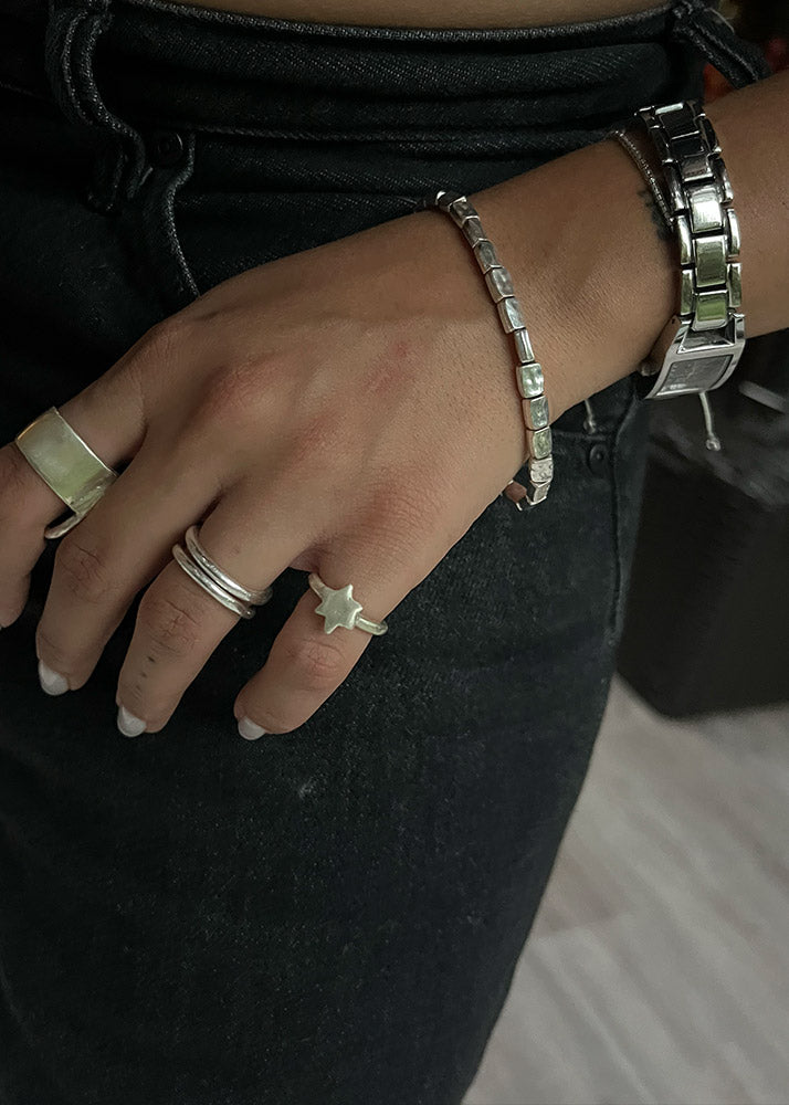 Close-up of a hand wearing multiple silver rings and bracelets on a dark background