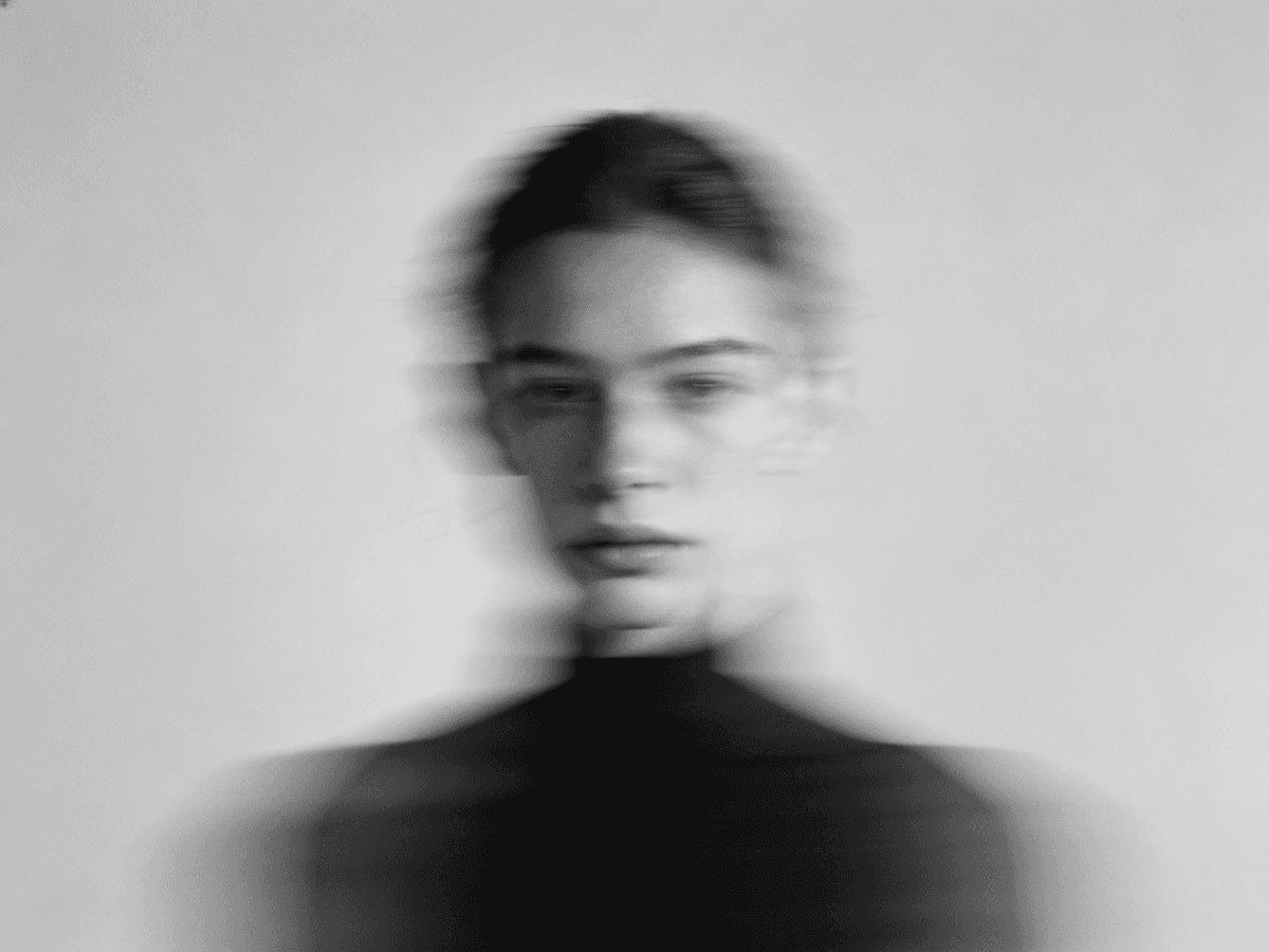 A black and white, motion-blurred portrait of a person wearing a dark turtleneck, evoking a mysterious and cinematic aesthetic.