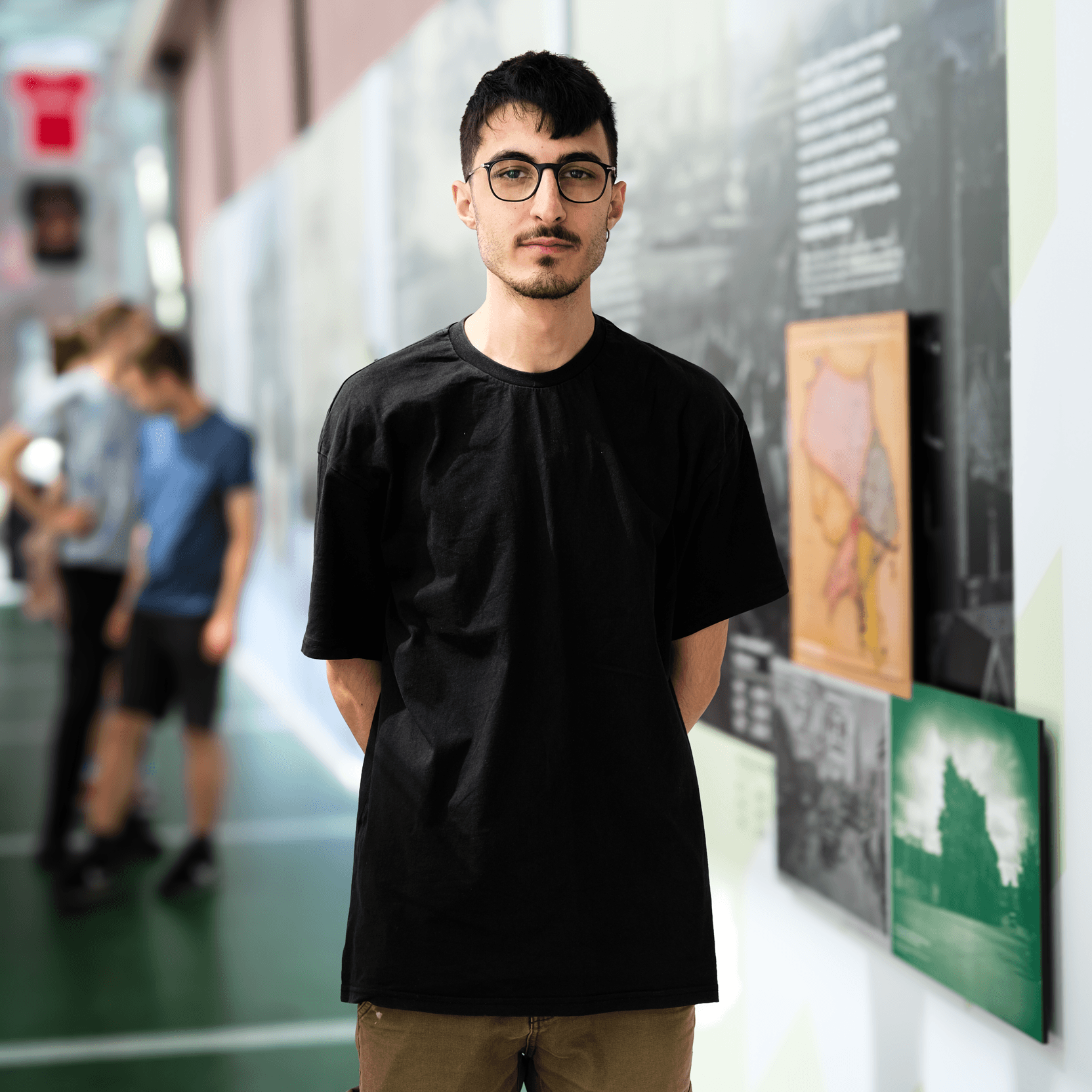 Angelo Tanzillo standing calm and direct, beside an exhibition wall in a busy gallery.