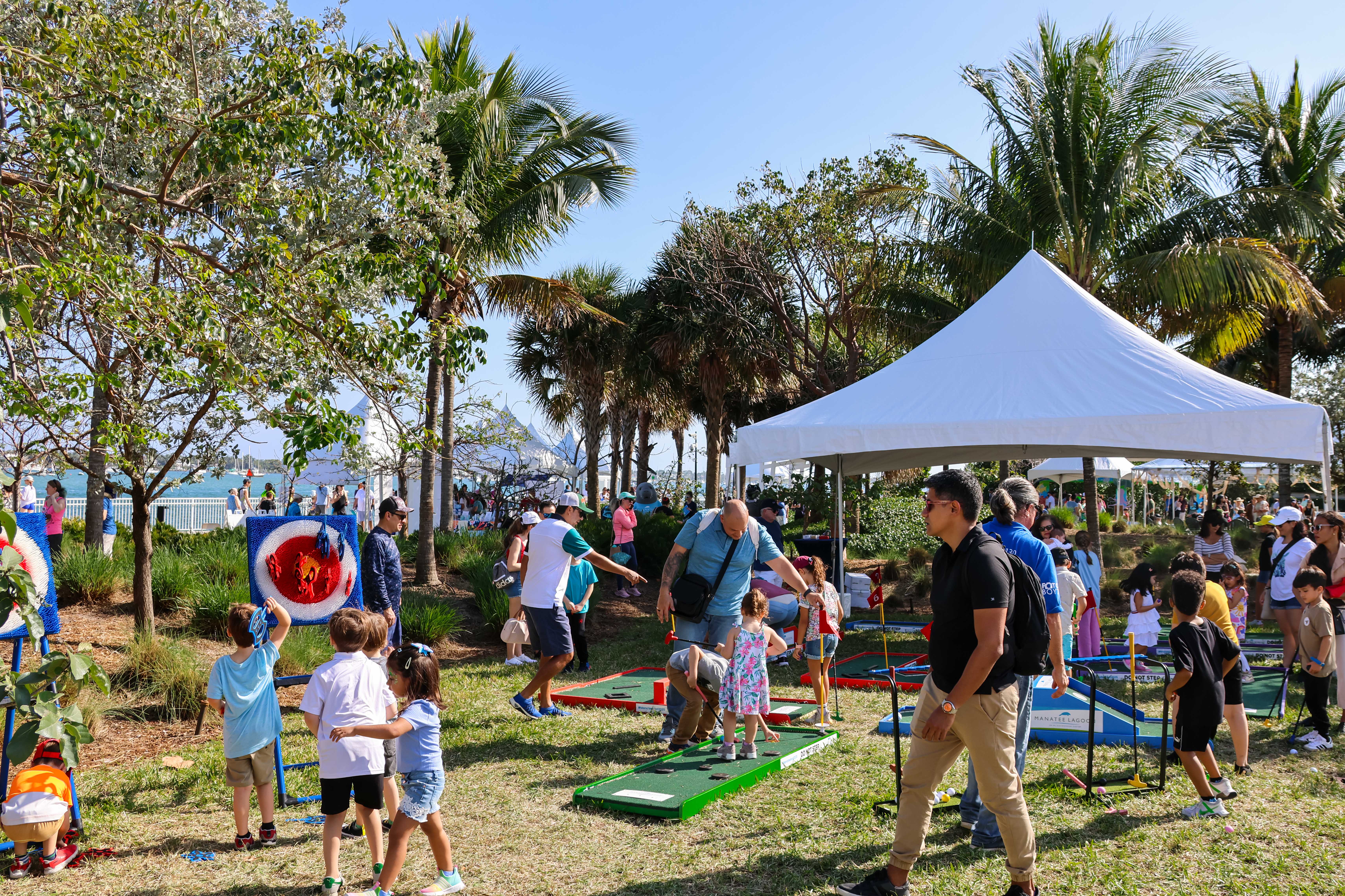 Outdoor family event with kids playing games under a white tent near palm trees.