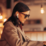 Woman wearing sunglasses and wireless earbuds working on laptop