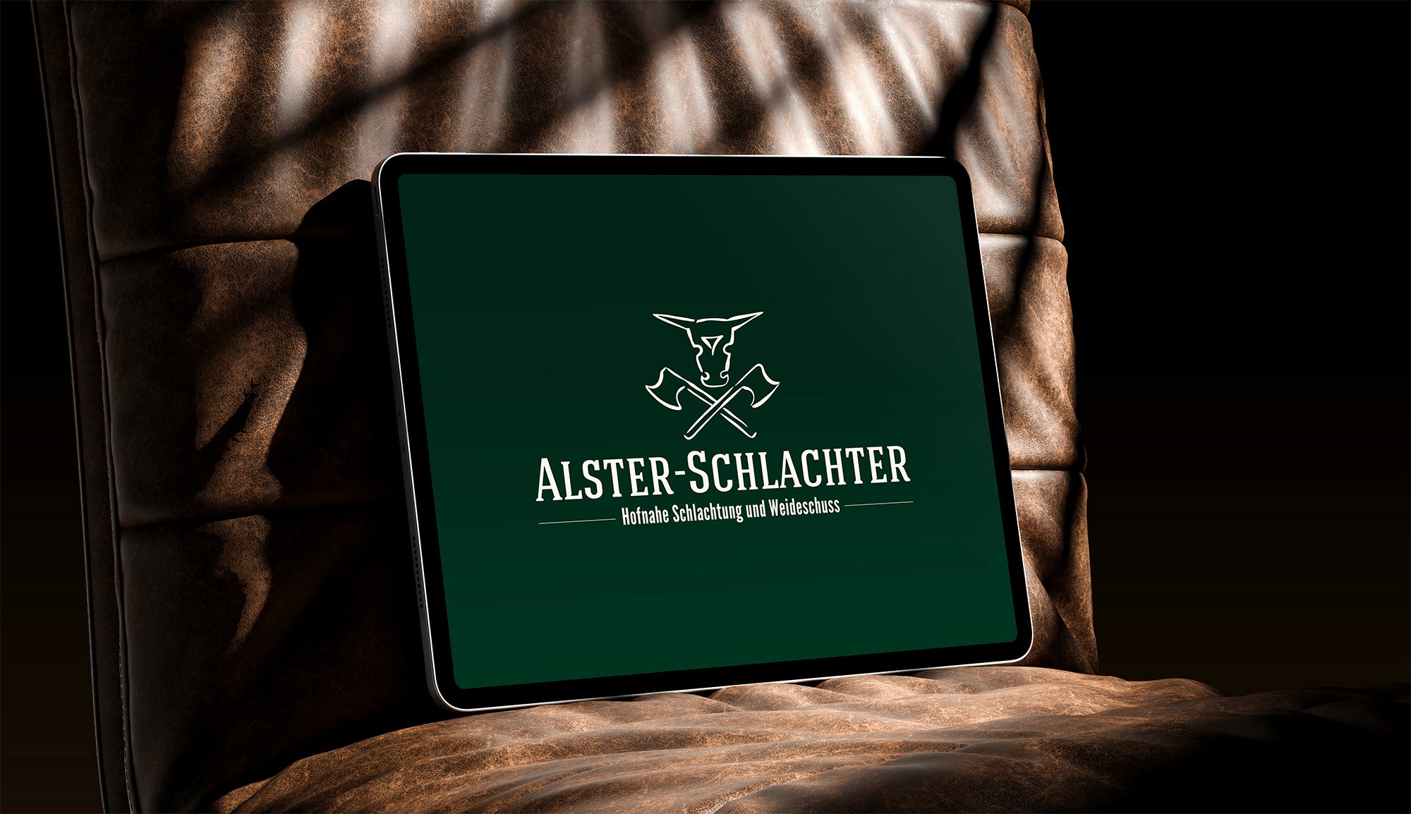 Tablet zeigt das Logo vom „Alster-Schlachter“, gestaltet von Storch Designstudio, auf weinrotem Hintergrund. Das Logo in Beige zeigt einen stilisierten Stierkopf und zwei gekreuzte Äxte. Das Tablet lehnt auf einem Ledersessel.