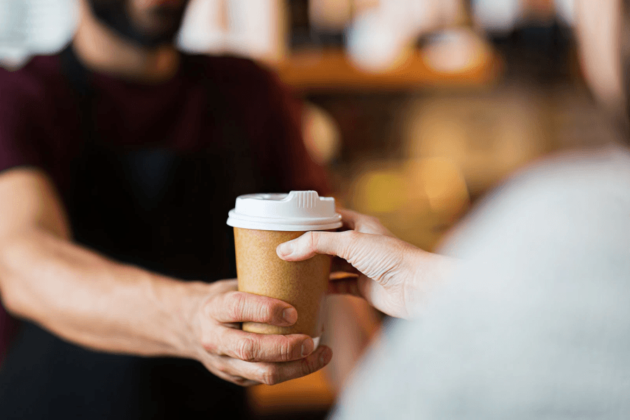 Barista handing a takeaway coffee cup to a customer in an Australian café, highlighting convenience and sustainability choices.