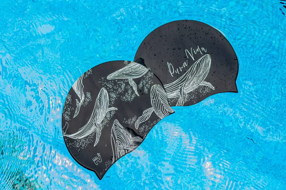 Dos gorras negrascon ilustraciones de ballenas sombre el agua