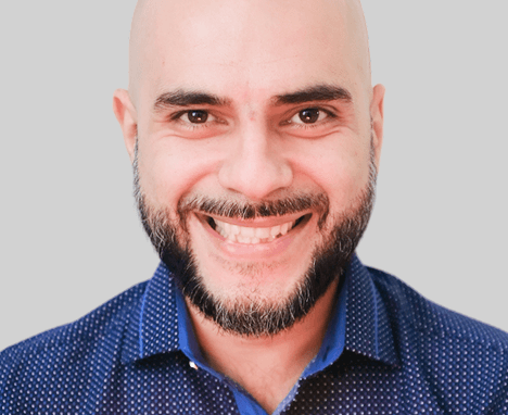 Minimal studio portrait of a confident woman in a white shirt, arms crossed, on a soft gray background.