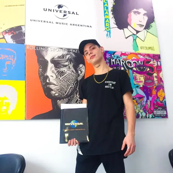 A young man stands in front of a wall featuring a collection of album covers, likely promoting Universal Music Argentina.
