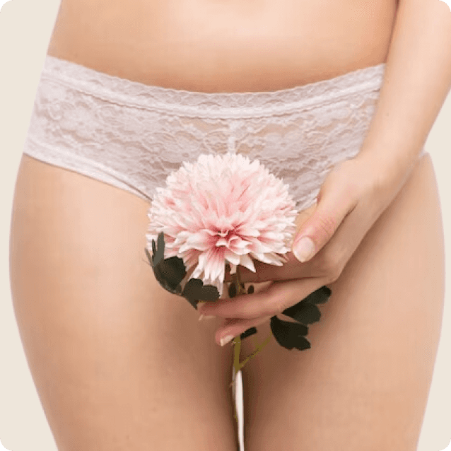 Close-up of a young woman gently holding a flower near her vaginal area, symbolizing femininity and self-care. The image conveys a sense of empowerment and confidence, emphasizing the theme of vaginal rejuvenation and personal well-being. The soft lighting and focus on the flower add a serene and delicate touch to the composition.