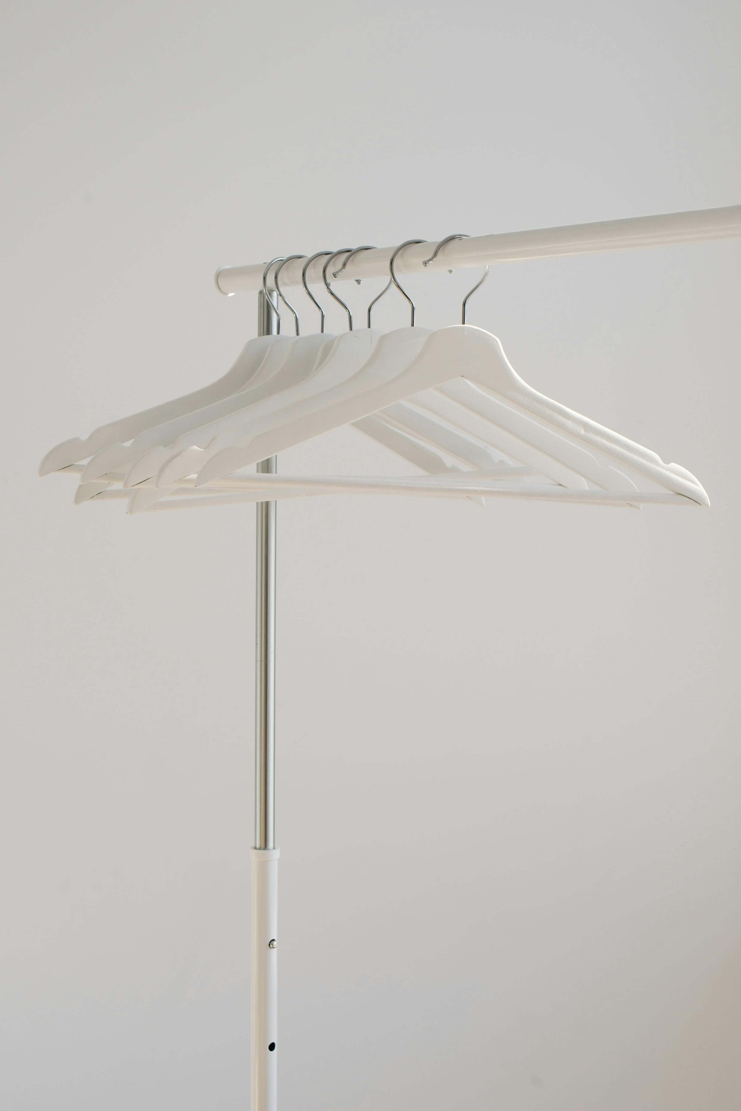 An empty clothing rack with several white hangers neatly arranged on the rail. The background is a plain white wall.