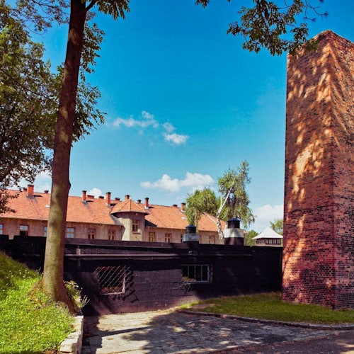 Brick building with a large chimney, adjacent trees, and a courtyard area under a clear blue sky.