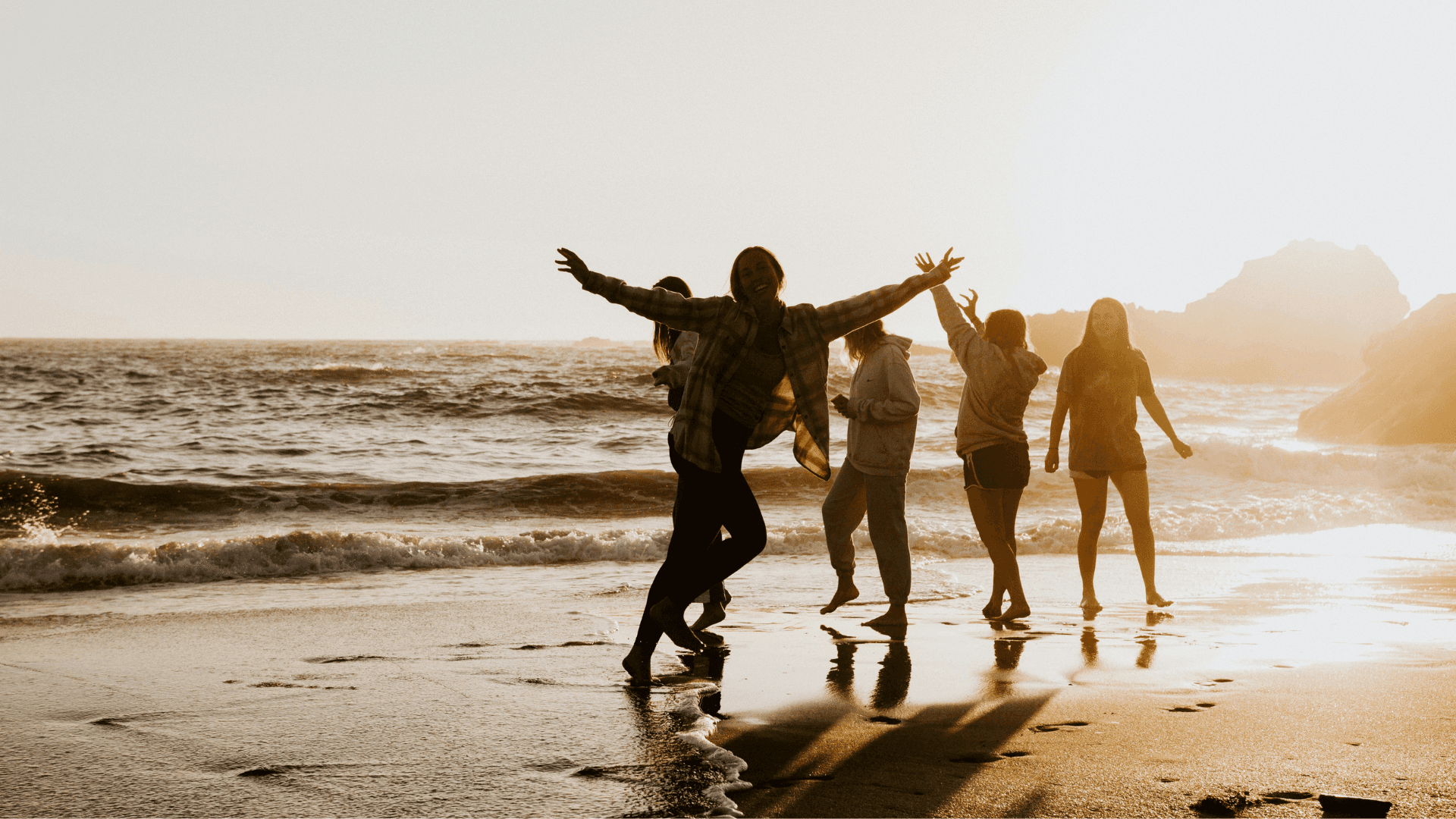 A group of people running and jumping on a beach at sunset